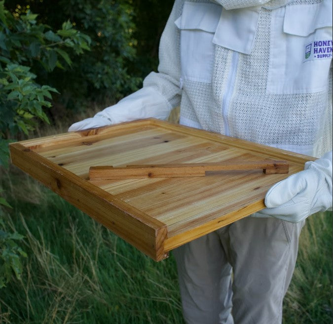 Man in a bee suit holding a wax dipped bottom board for a beehive.