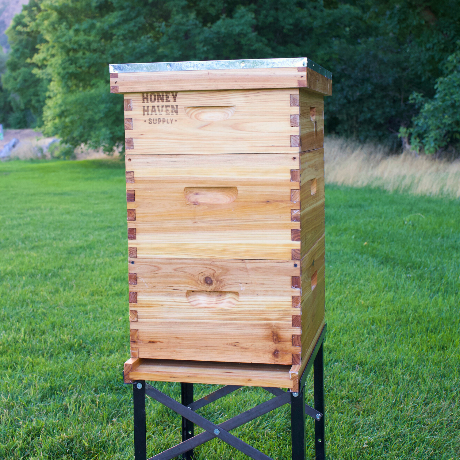 A full wax dipped Honey Haven Supply beehive sits on a hive stand in a green grass field.