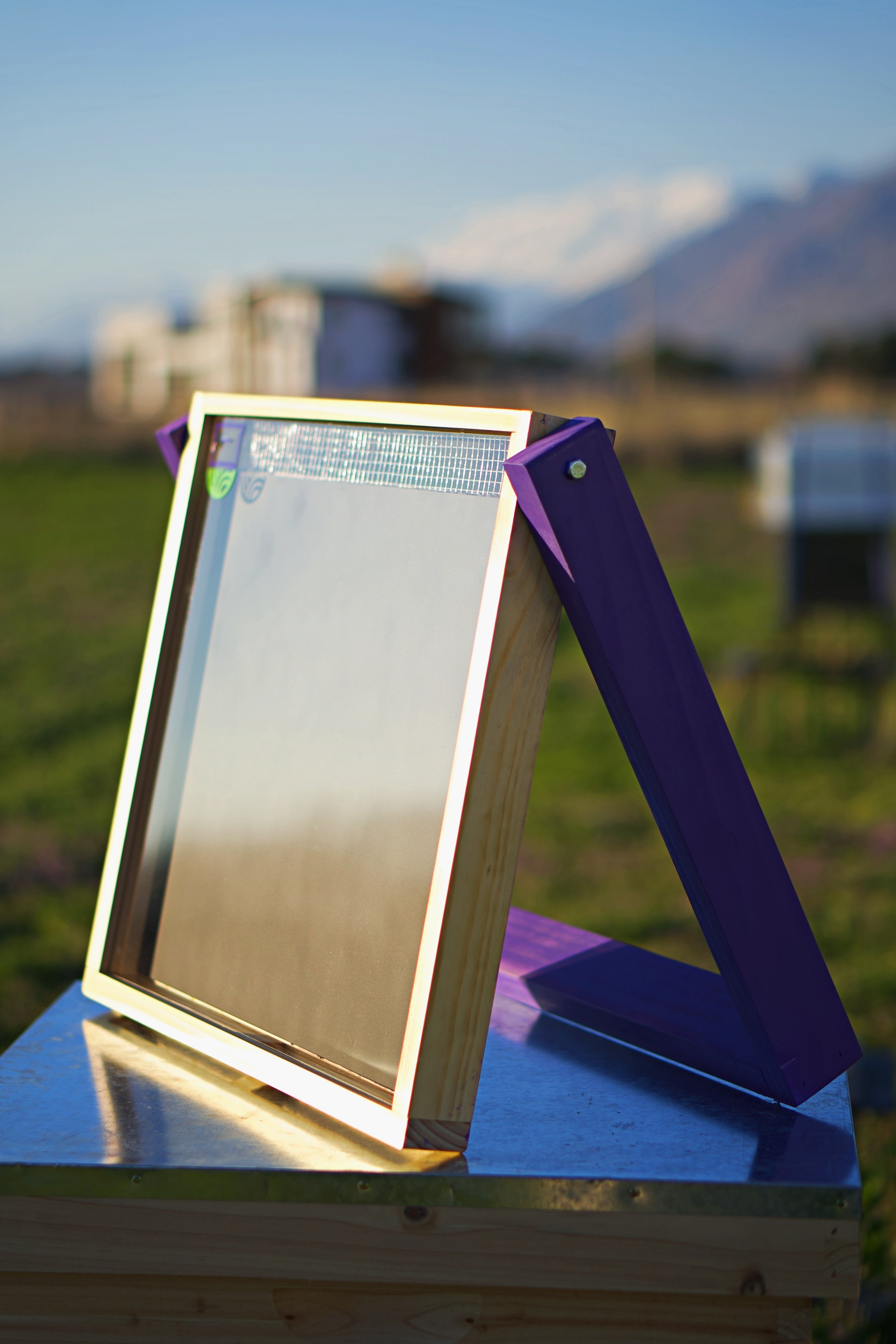 A HiveHeater is displayed sitting on top of a hive with the reflection of the sun in the glass.