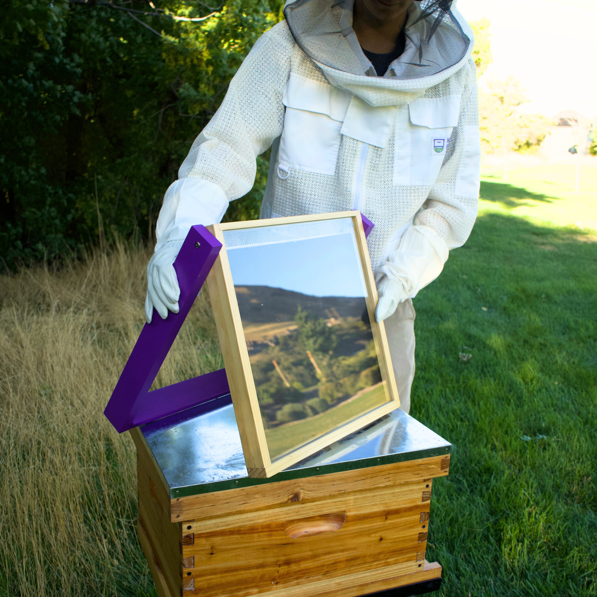 A HiveHeater sits on the top of a double wax dipped hive to display the HiveHeater. A man in a beekeeping jacket steadies the HiveHeater.