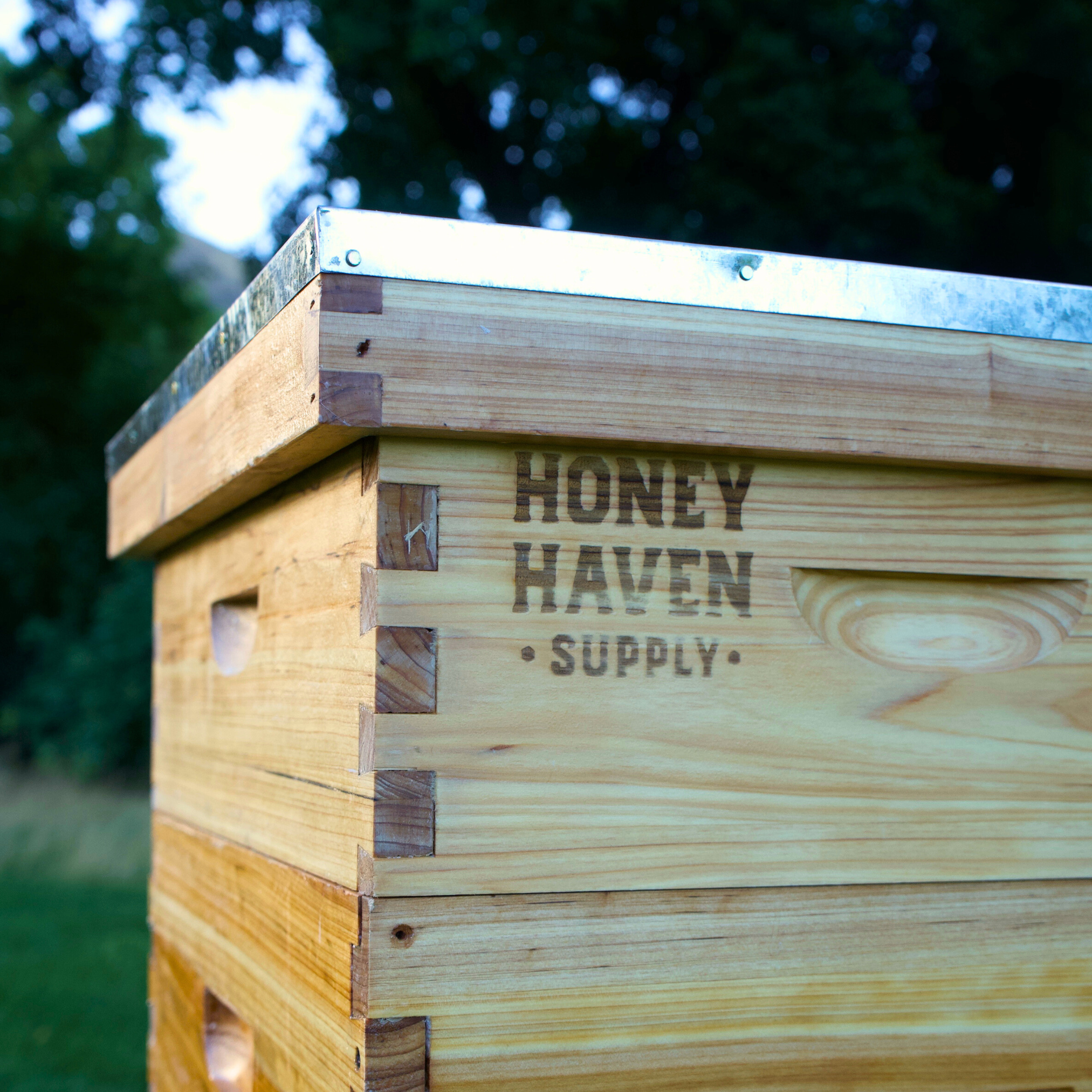 Close up of a beehive with a lid installed. The brand logo of Honey Haven Supply is laser engraved on the side of the hive. The lid and box are made from wax dipped pine.