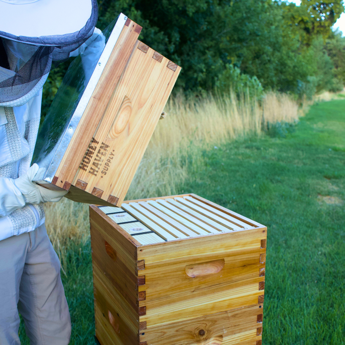 Man in bee suit opening a hive to display and installed plastic internal bee feeder.